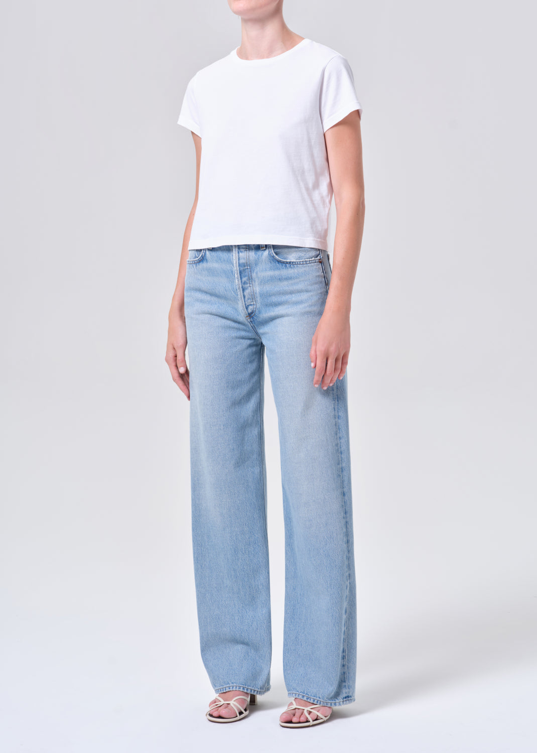 Person wearing light blue jeans and a white t-shirt on a plain background