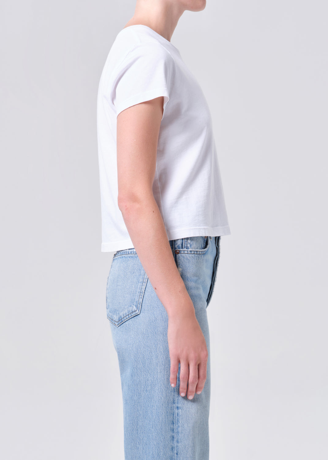 Person wearing a white t-shirt and light blue jeans on a plain background