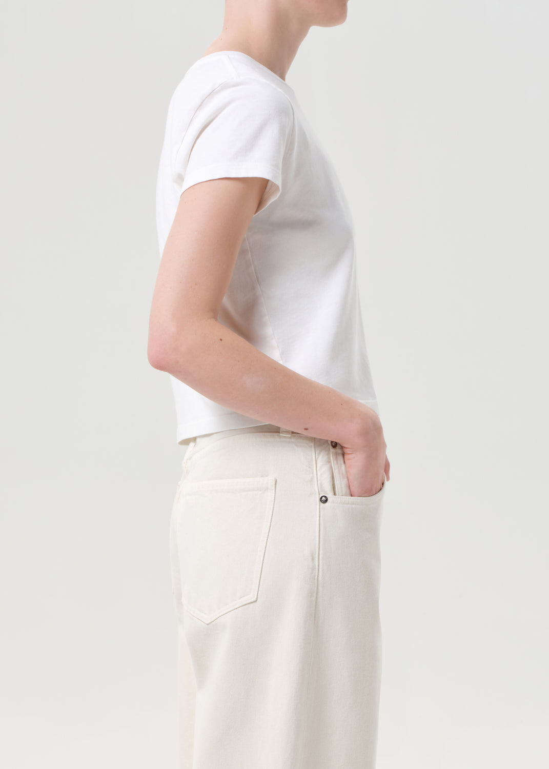 Person wearing a plain white t-shirt and light-colored pants on a light background