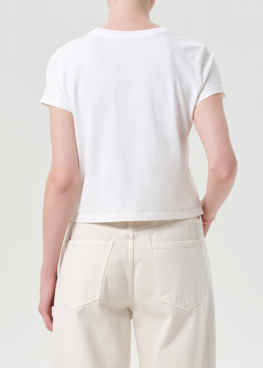 Person wearing a white t-shirt and light-colored pants on a plain background