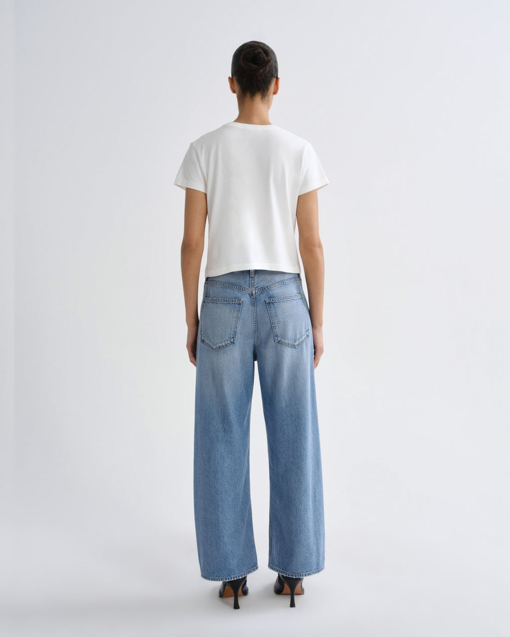 Person wearing a white t-shirt and blue jeans on a plain background