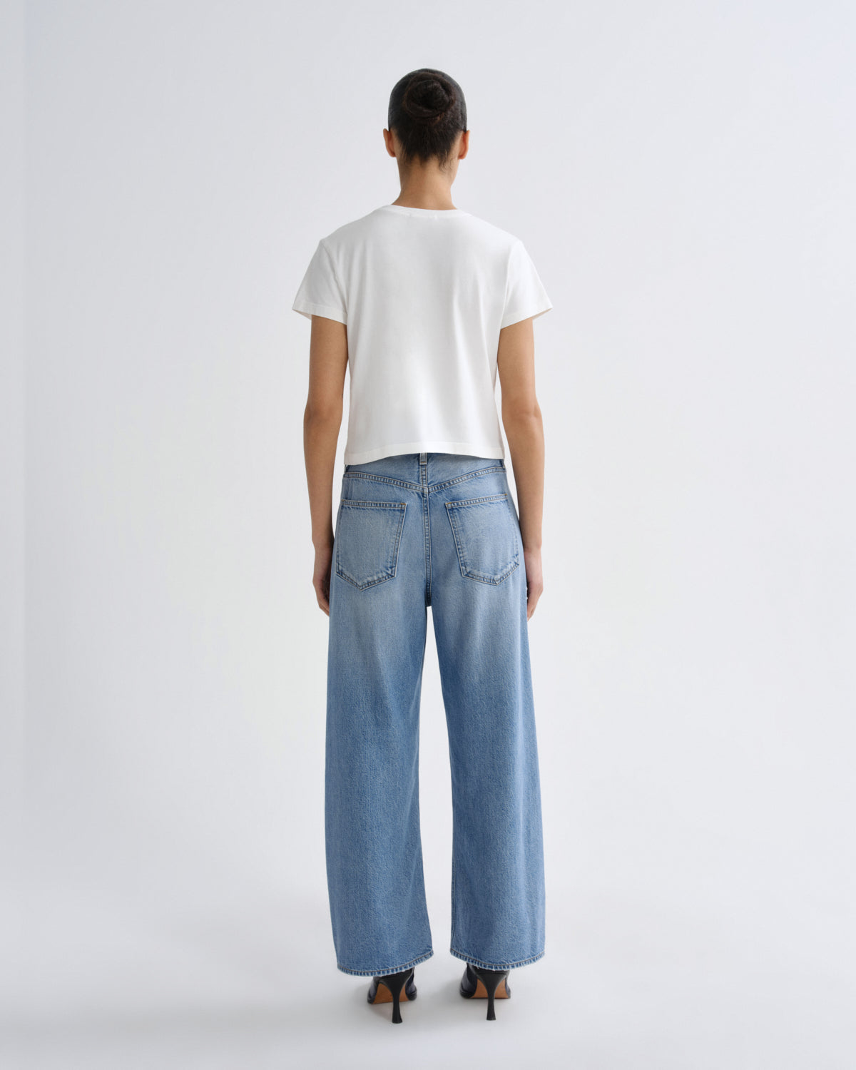 Person wearing a white t-shirt and blue jeans on a plain background