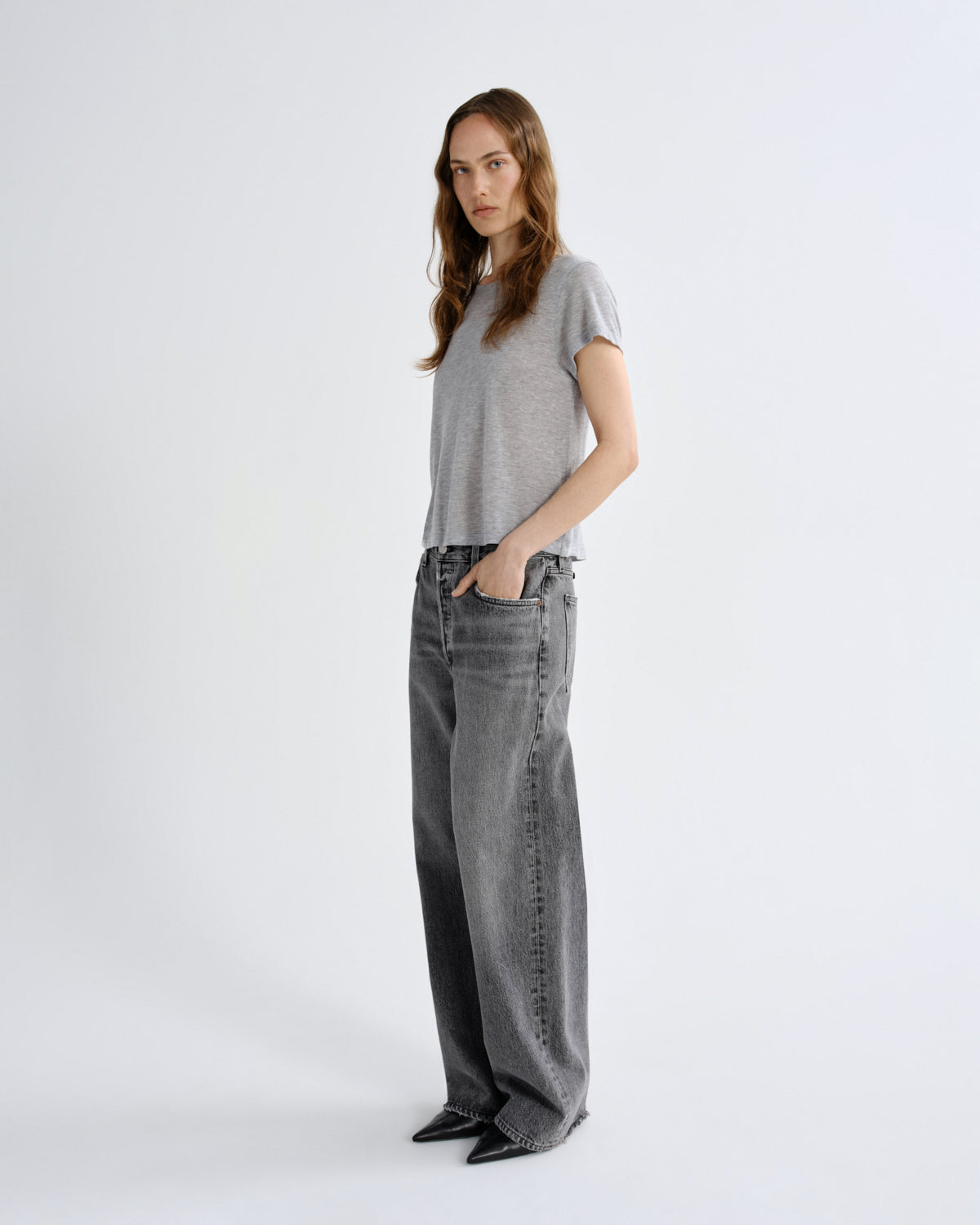 A woman modeling a light gray short-sleeve knit top and wide-leg gray jeans against a clean white studio background.