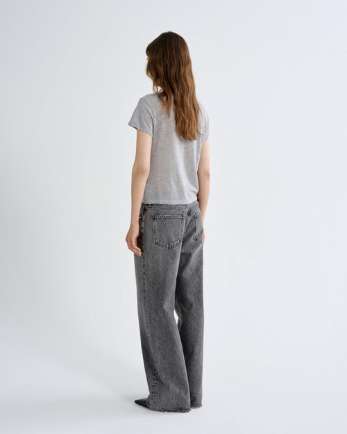 A woman viewed from the back wearing a light gray short-sleeve t-shirt and dark gray wide-leg jeans, standing against a plain light gray studio background.