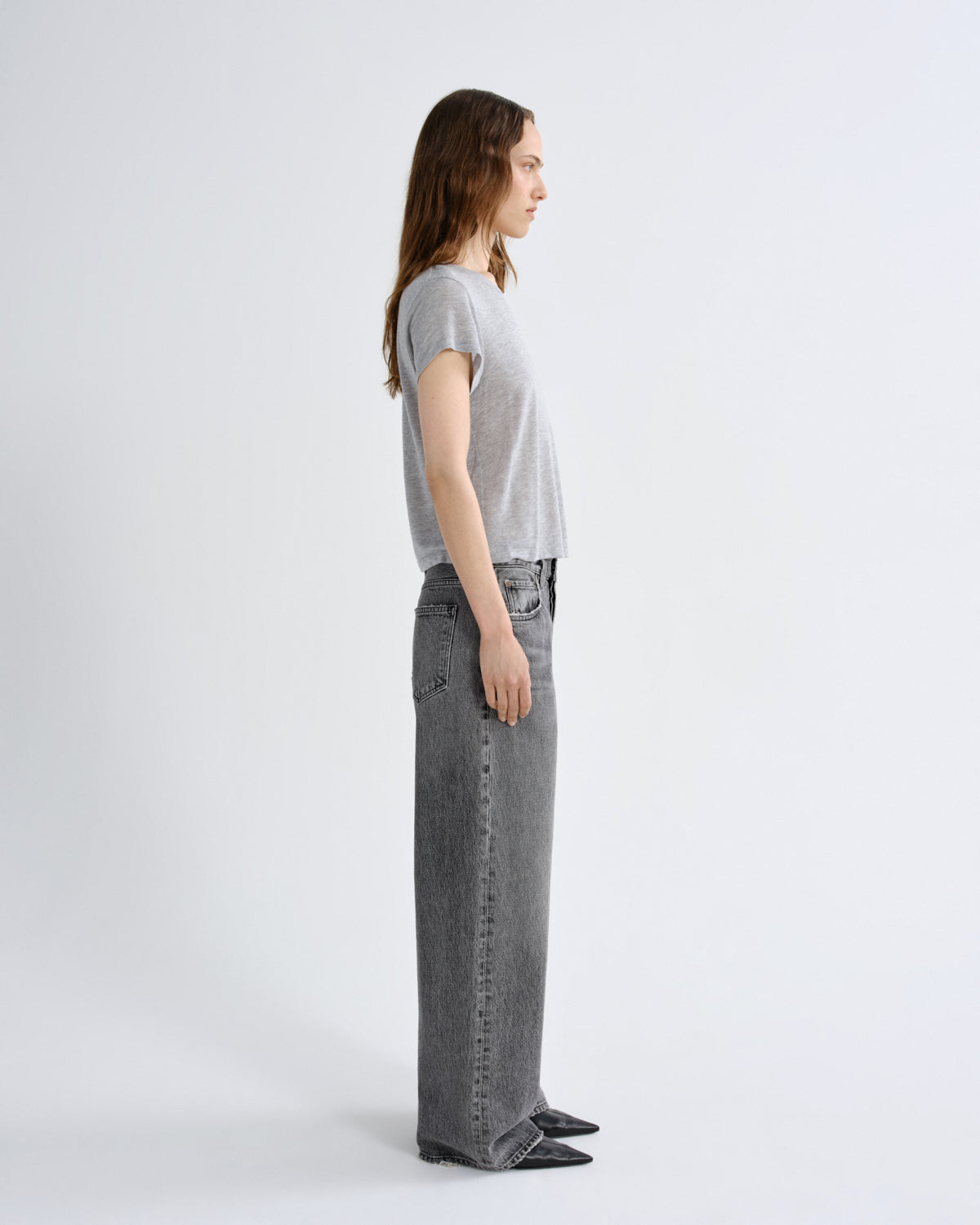 A model shown in profile wearing a light gray short-sleeve t-shirt and wide-leg gray jeans against a plain light gray studio background.