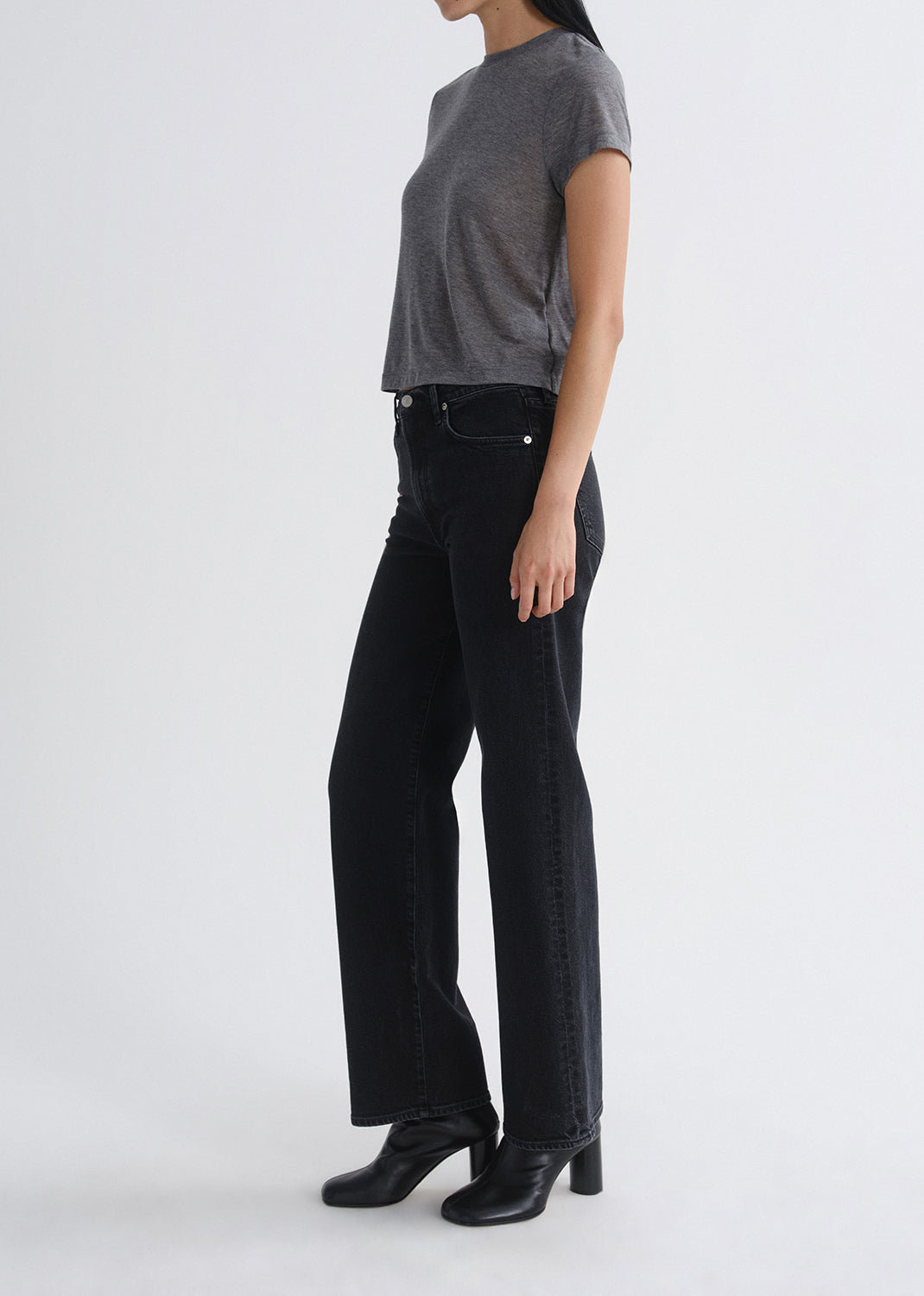Person wearing black jeans and a grey top on a grey background