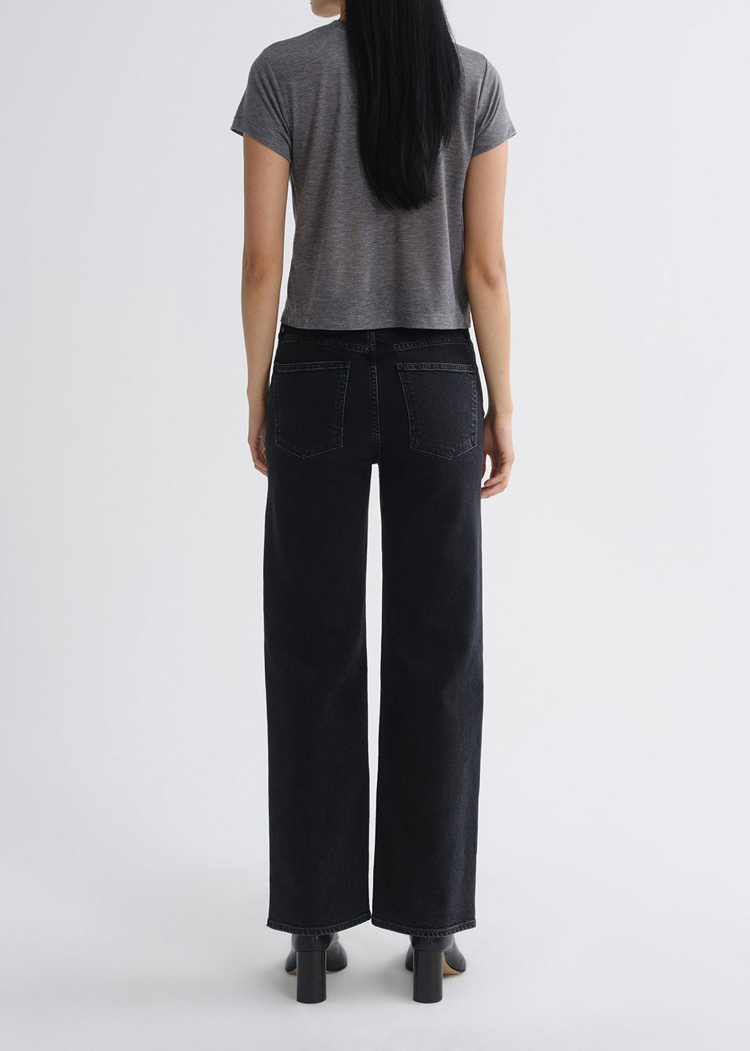 Person wearing black wide-leg jeans and a grey t-shirt on a grey background