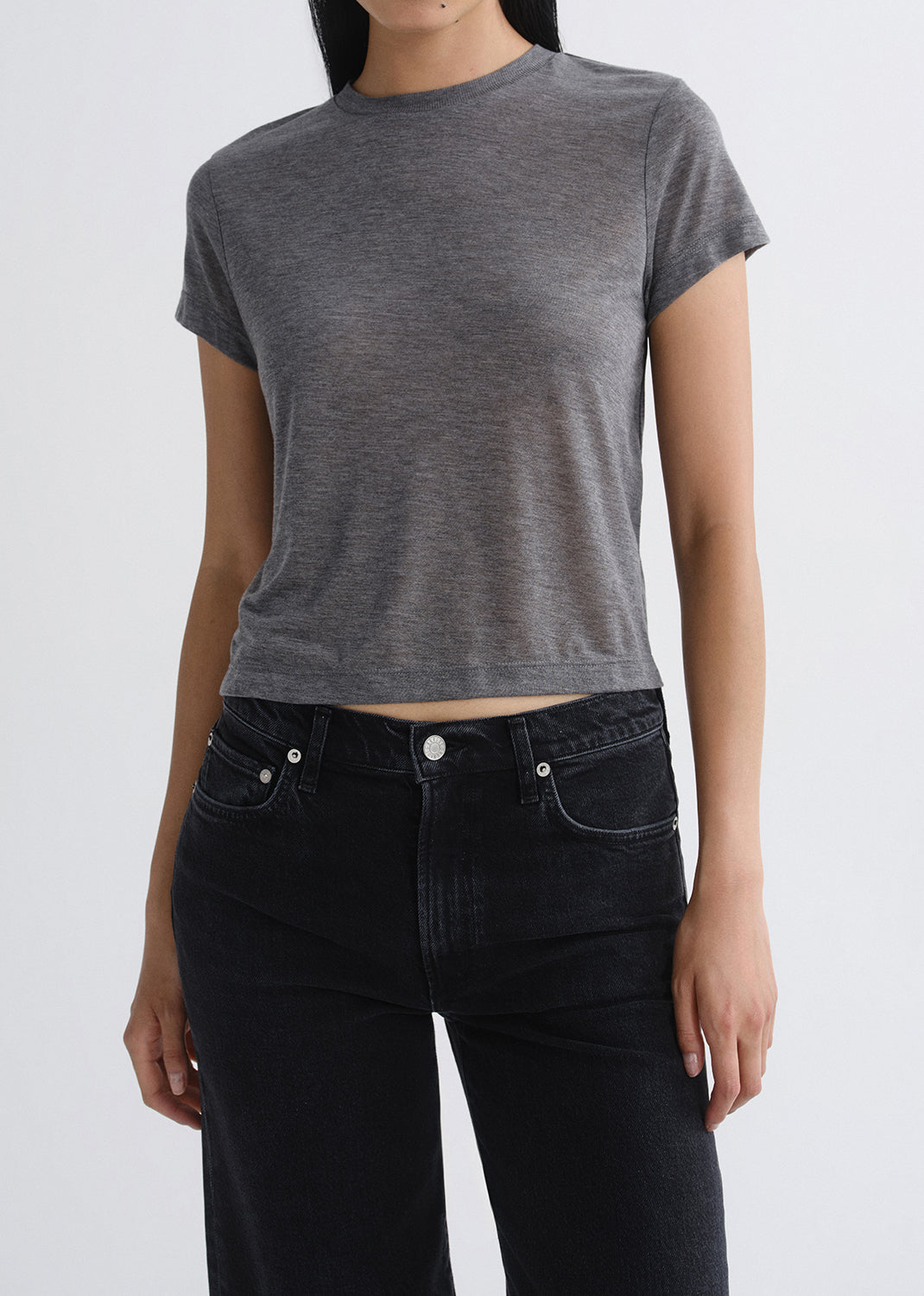 Person wearing a grey t-shirt and black jeans on a grey background