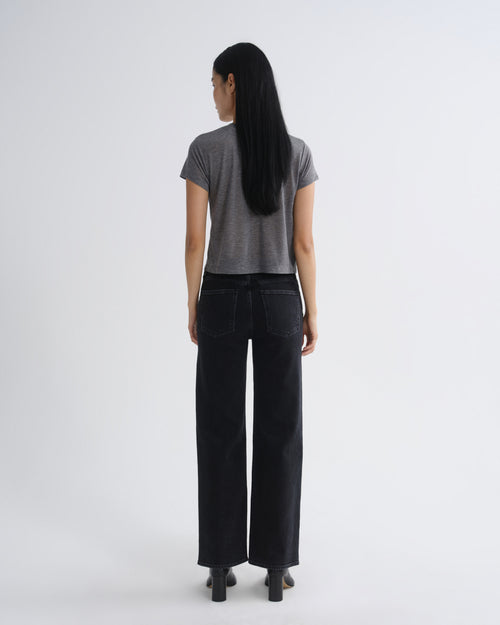A woman is shown from the back wearing a short-sleeve gray t-shirt and black wide-leg jeans against a plain light gray studio background.