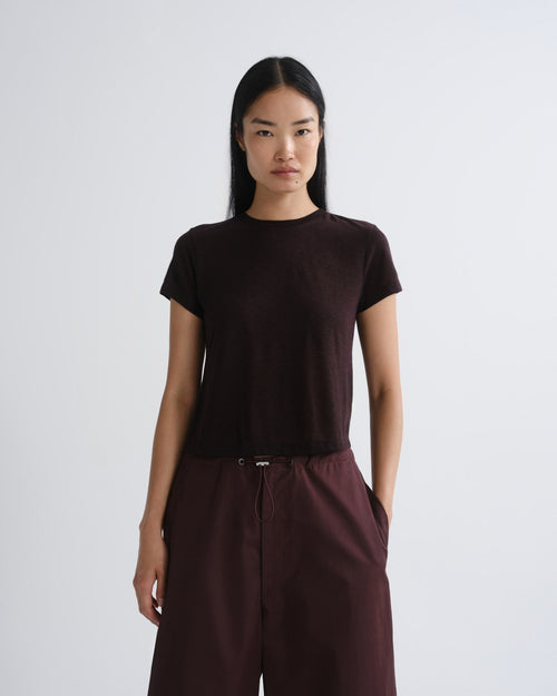 A model wearing a dark brown short-sleeve crewneck t-shirt and matching dark brown wide-leg trousers, standing against a light gray studio background.