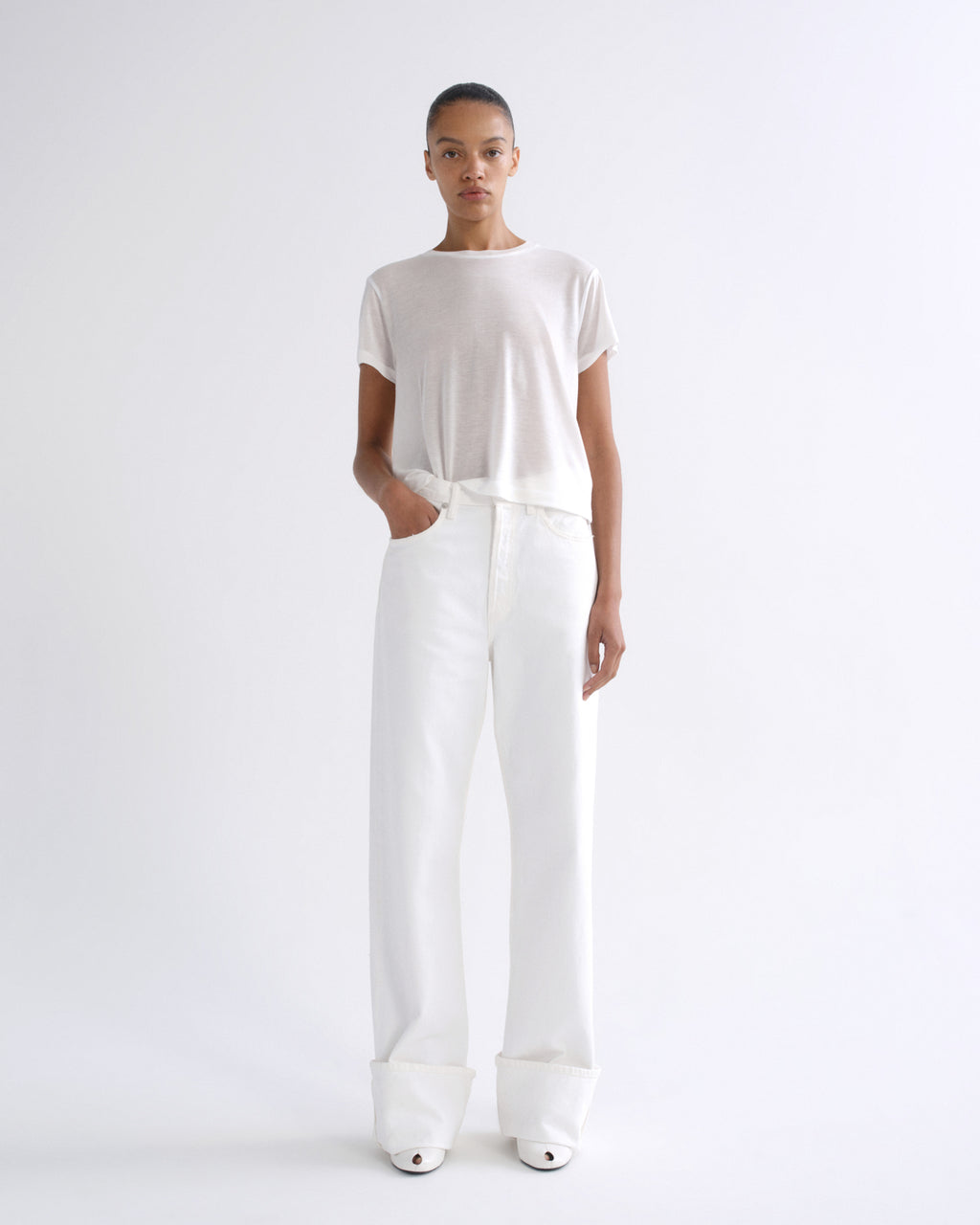 Woman wearing a white short sleeve crewneck tee with white straight leg pants on a grey background.