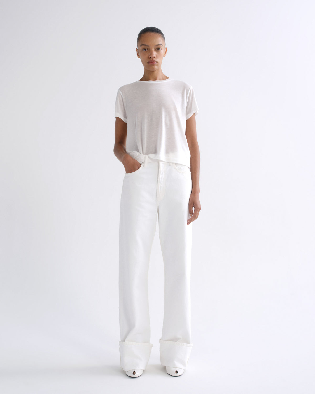 Woman wearing a white short sleeve crewneck tee with white straight leg pants on a grey background.