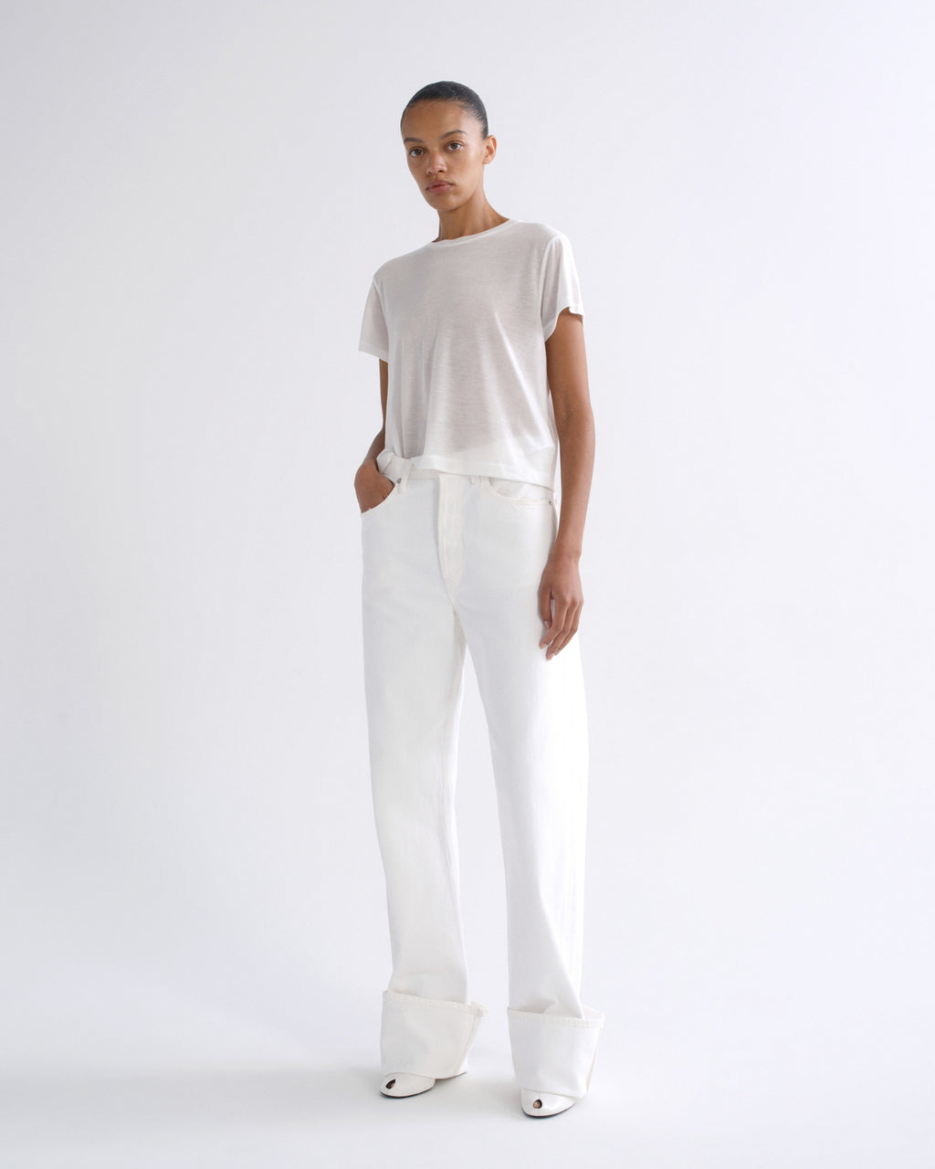 Woman wearing a white short sleeve crewneck tee with white straight leg pants on a grey background.