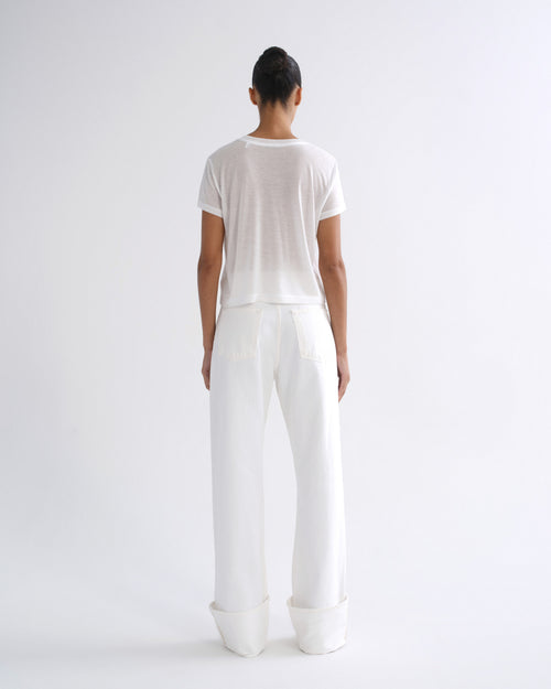 Woman wearing a white short sleeve crewneck tee with white straight leg pants viewed from the back on a grey background.