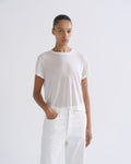 Woman wearing a white short sleeve crewneck tee with white straight leg pants on a grey background.