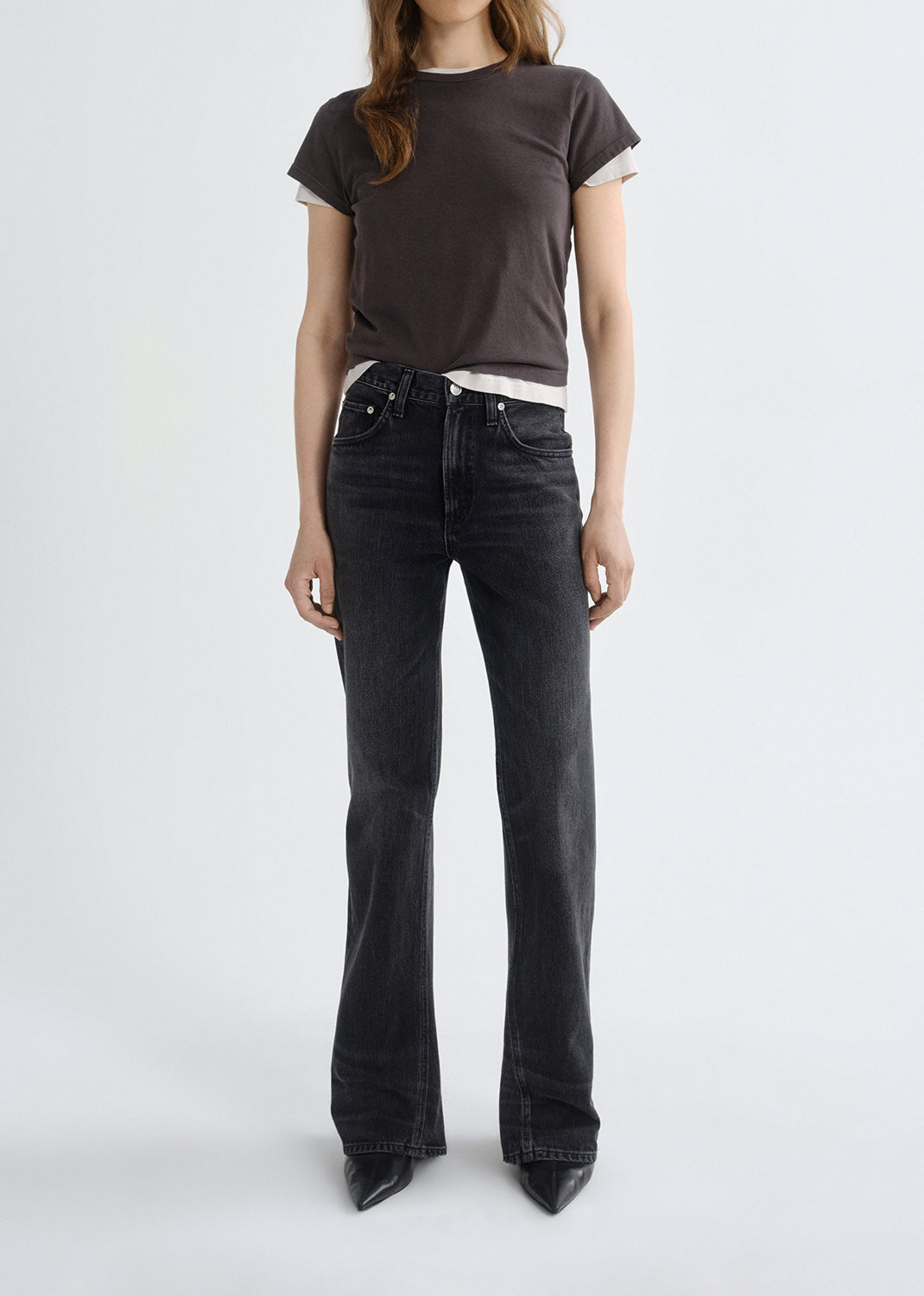 Person wearing a dark gray t-shirt and black flared jeans on a grey background