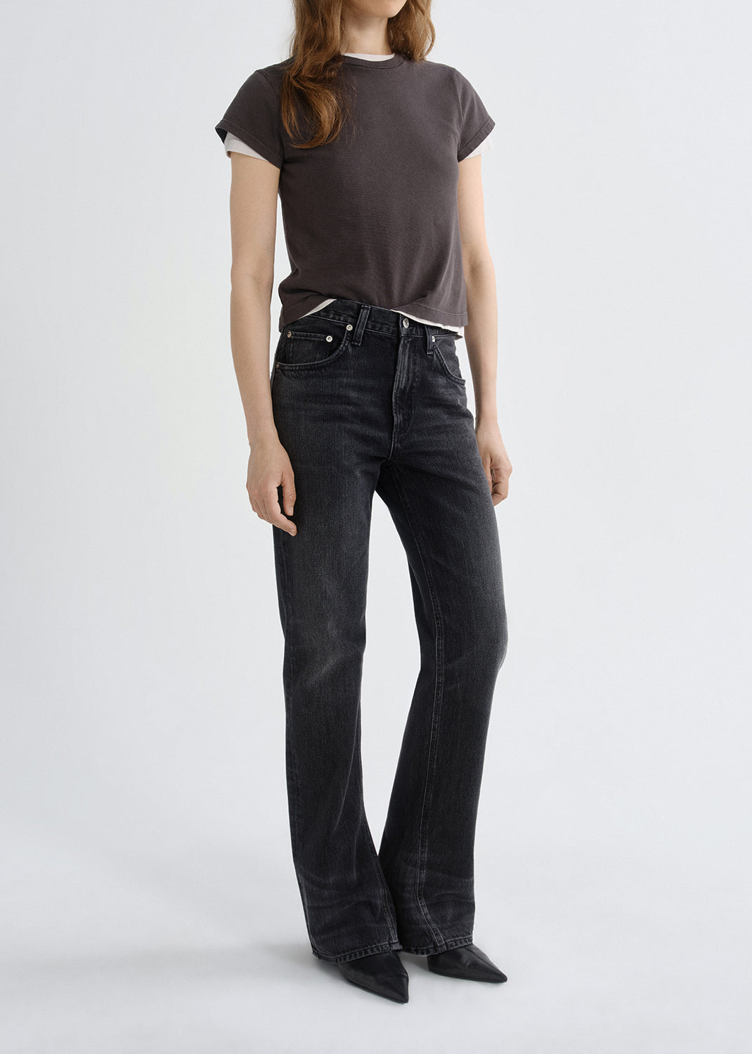 Person wearing a brown t-shirt and black flared jeans on a grey background