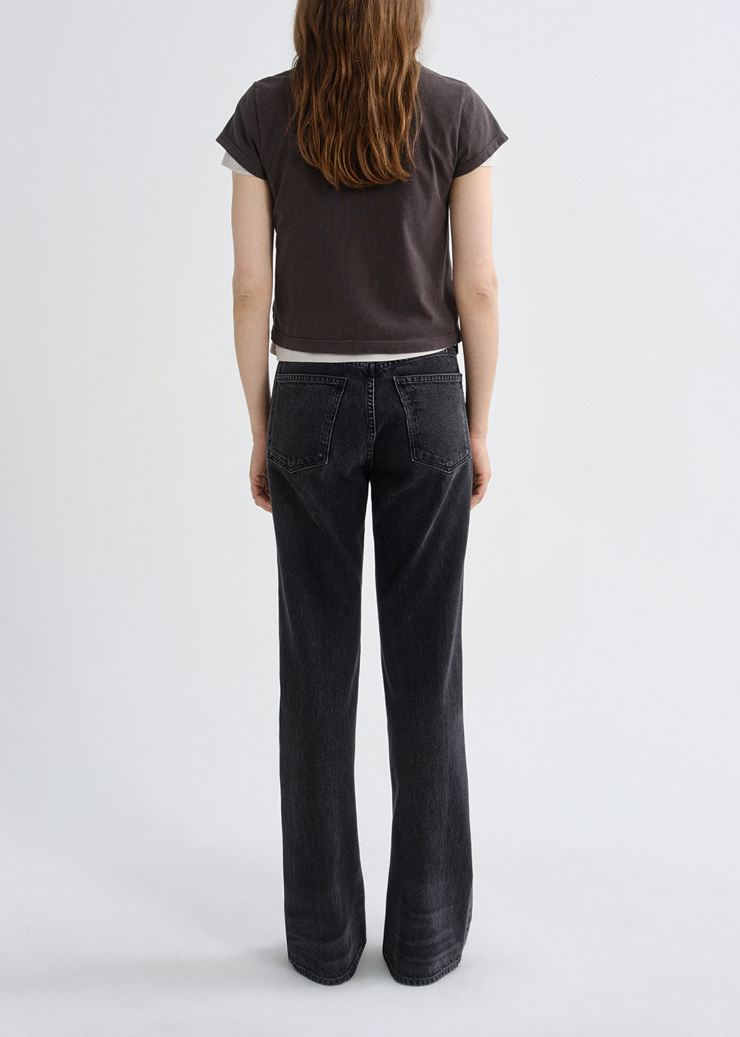 Person wearing black flared jeans and a brown t-shirt on a grey background