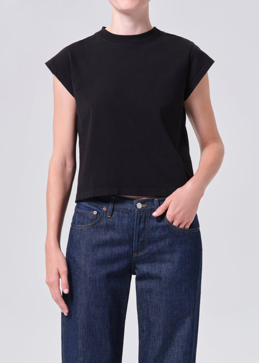 Person wearing a black crop top and blue jeans on a light gray background