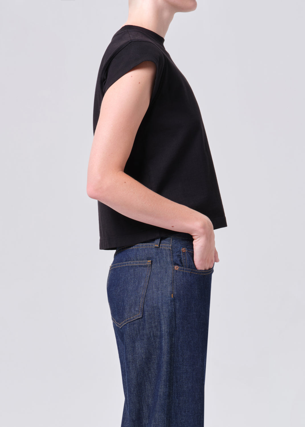 Person wearing a black sleeveless top and blue jeans on a light gray background