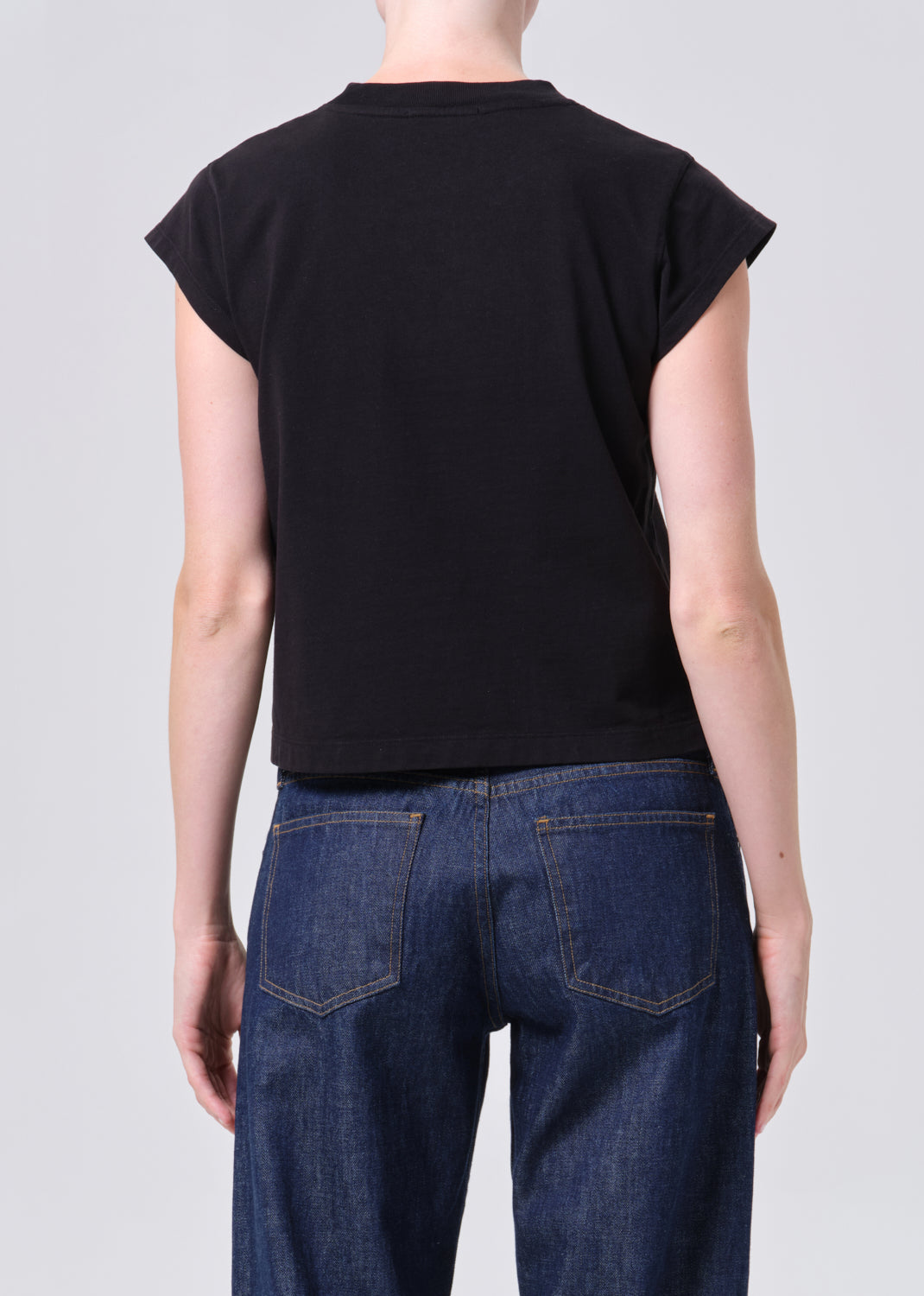 Person wearing a black sleeveless top and blue jeans on a plain background