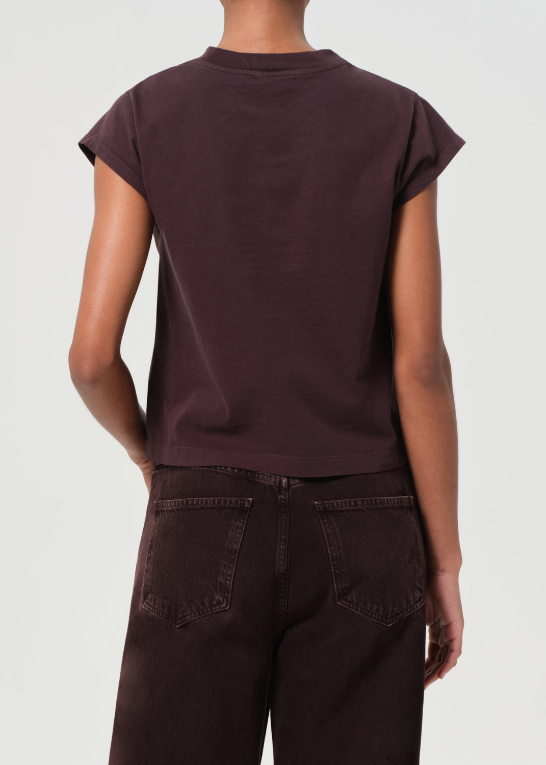 Person wearing a dark brown t-shirt and pants on a light gray background