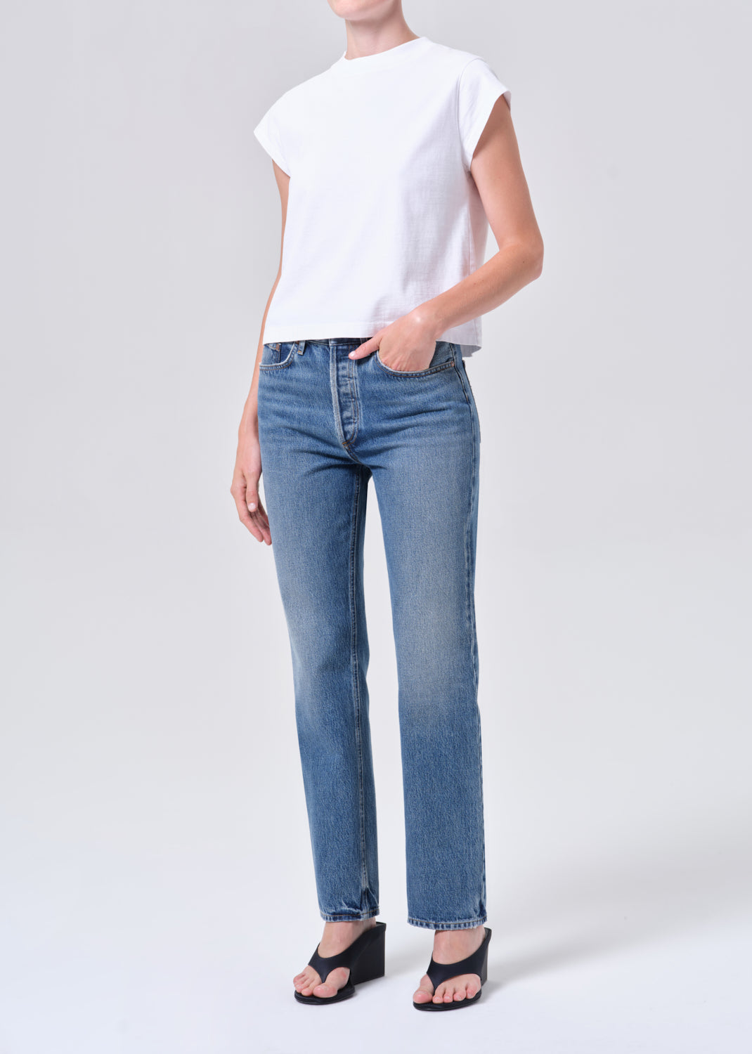 Person wearing a white top and blue jeans on a plain background