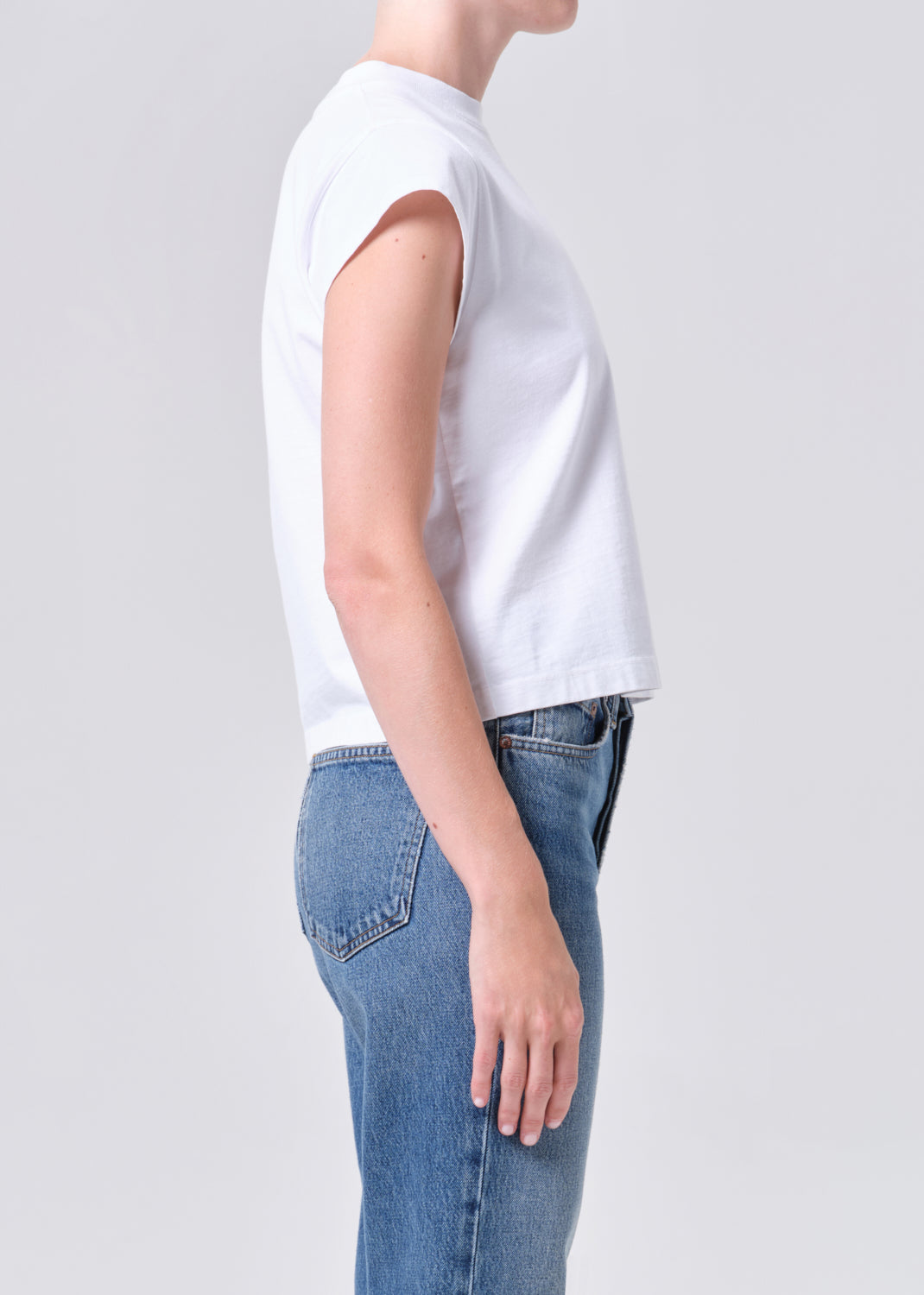 Person wearing a white sleeveless shirt and blue jeans on a plain background