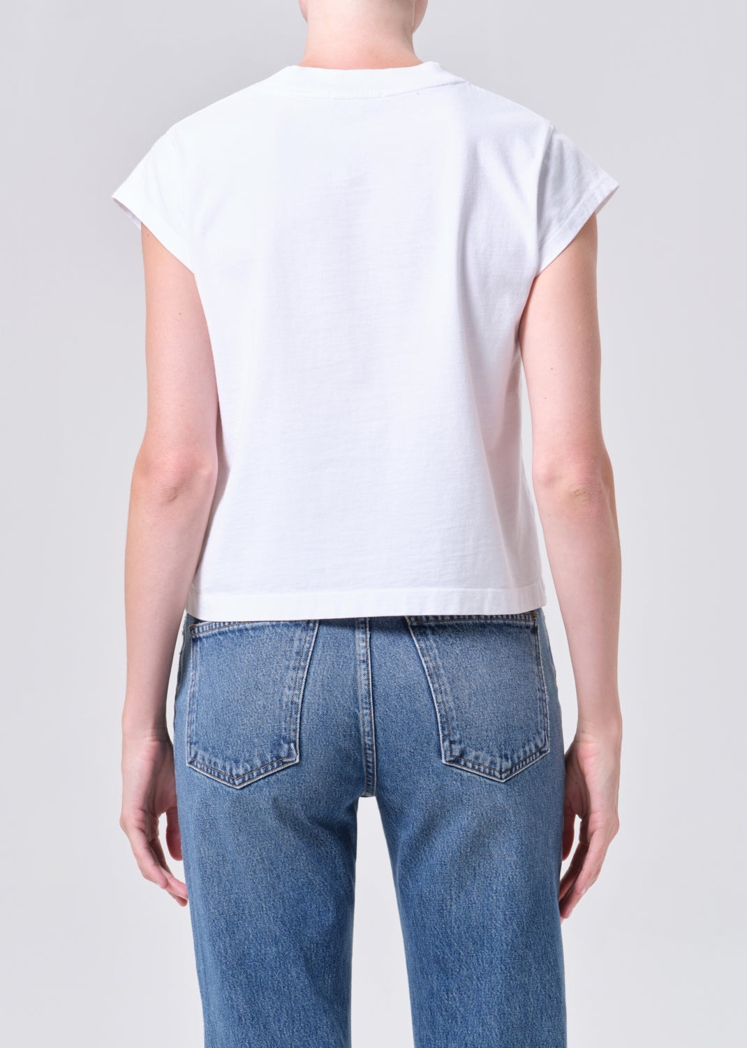 Person wearing a white t-shirt and blue jeans on a plain background