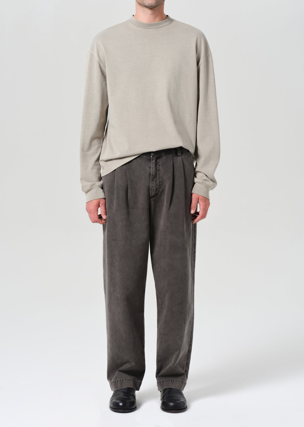 Person wearing a beige long-sleeve shirt and gray pants on a white background