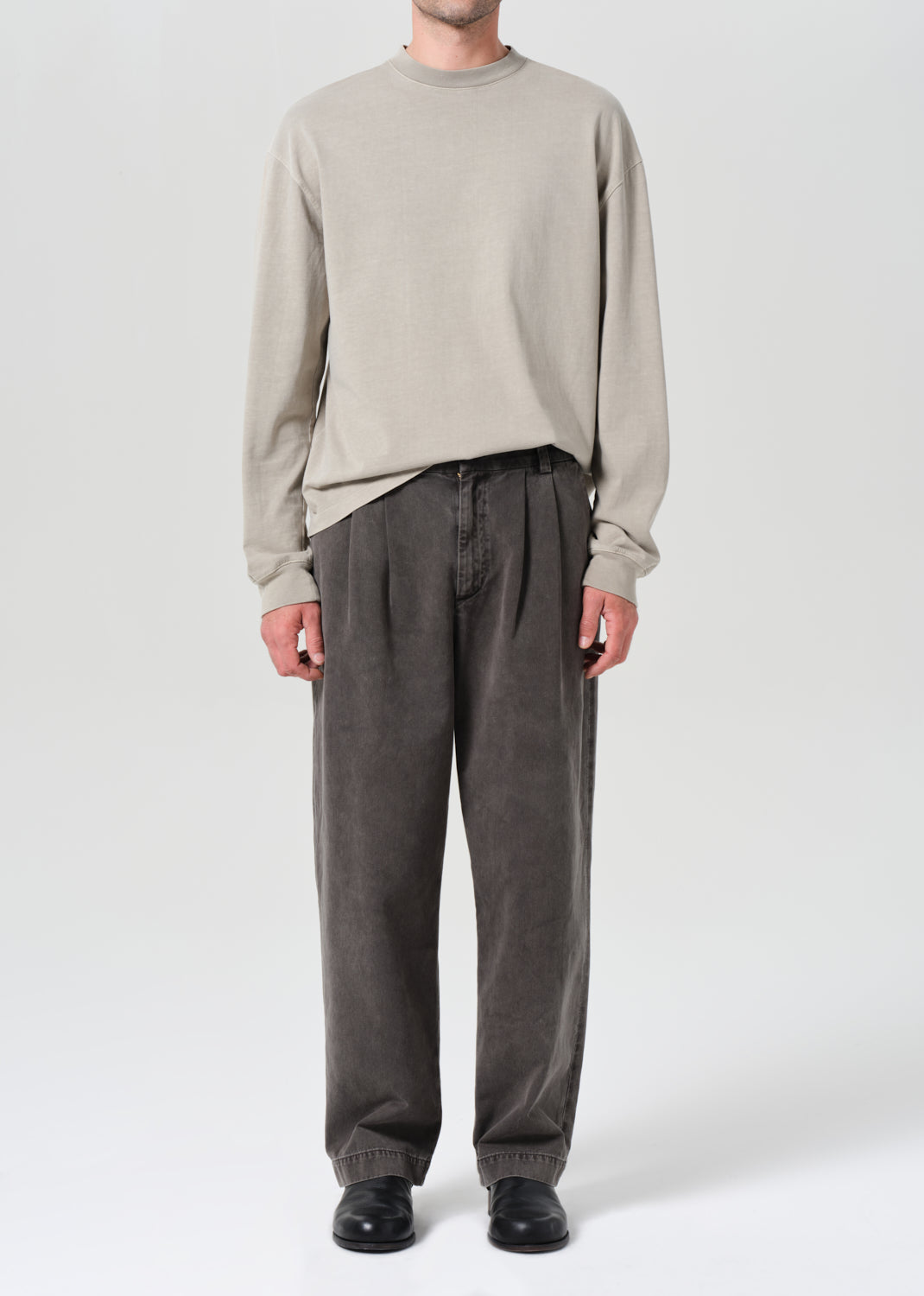Person wearing a beige long-sleeve shirt and gray pants on a white background