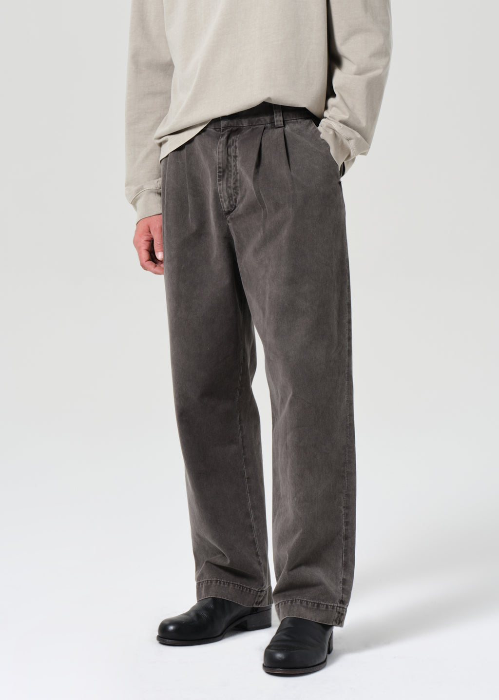 Person wearing gray pleated pants and a beige shirt on a white background