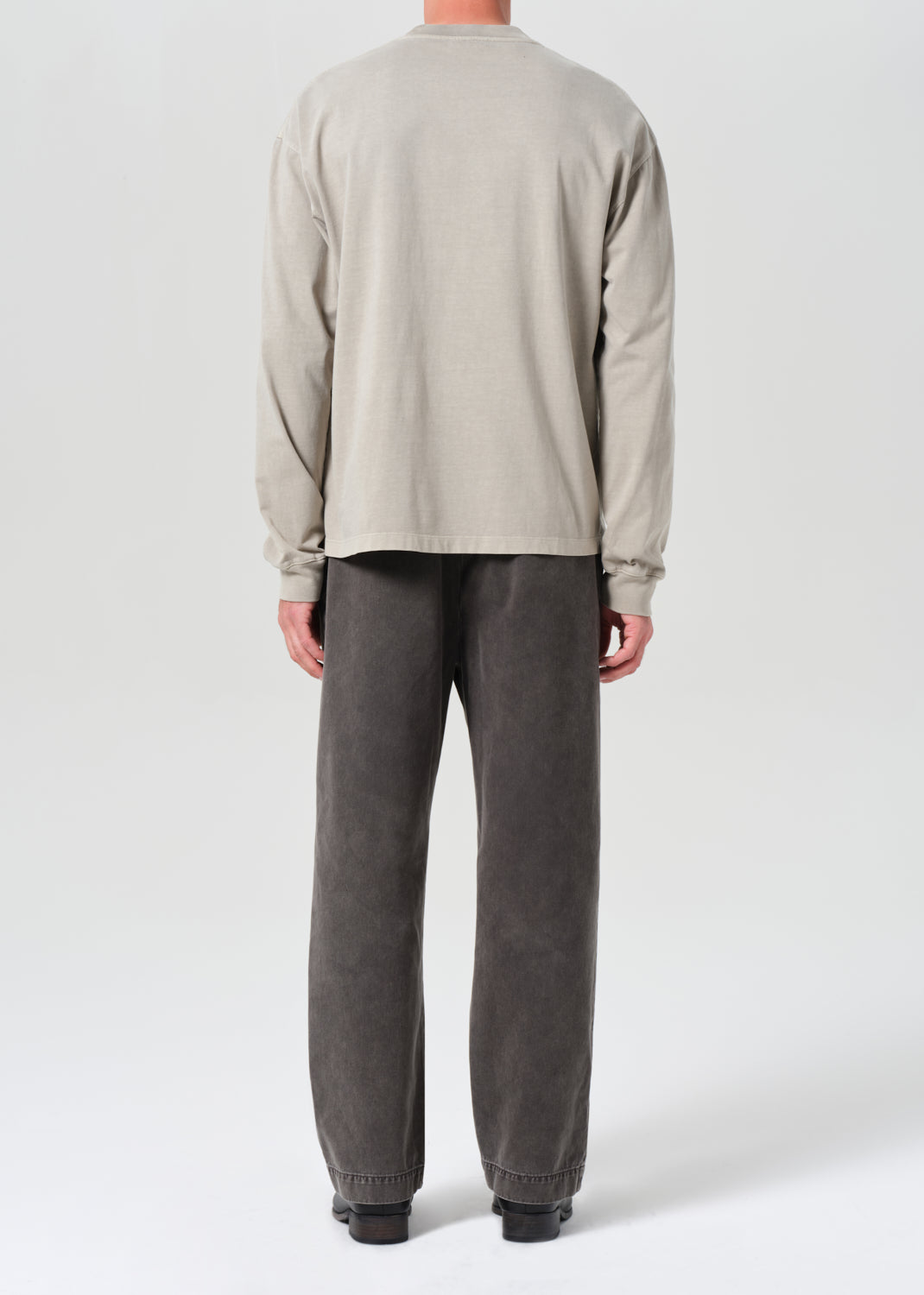 Person wearing a beige long-sleeve shirt and gray pants on a white background