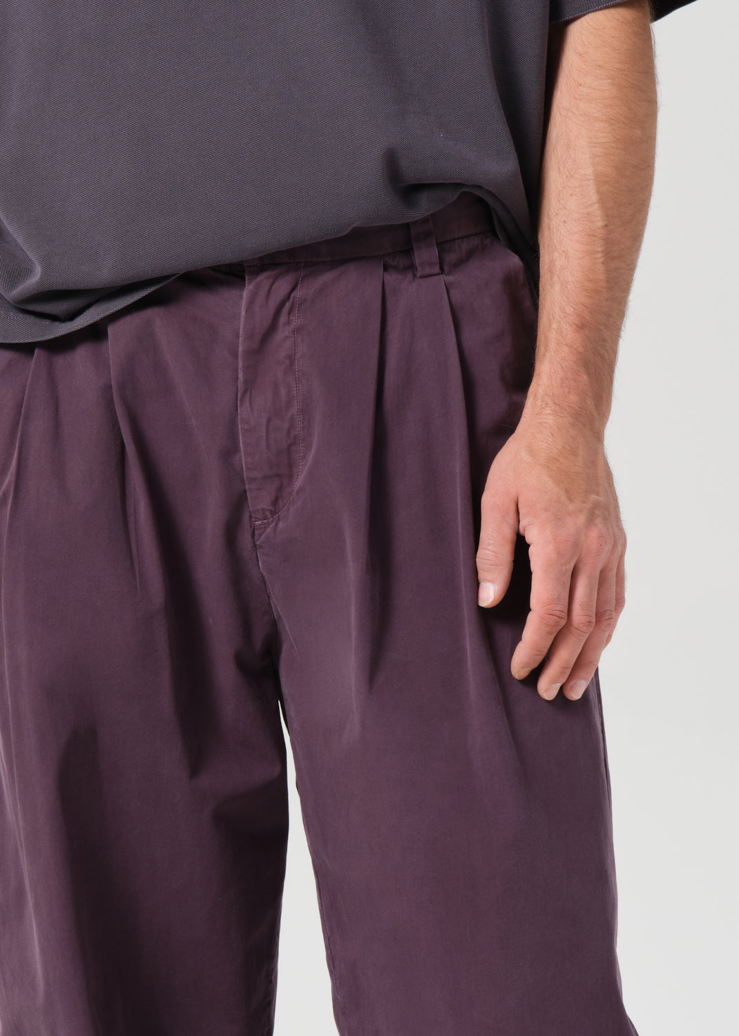 Person wearing purple pleated pants and a dark shirt on a light gray background