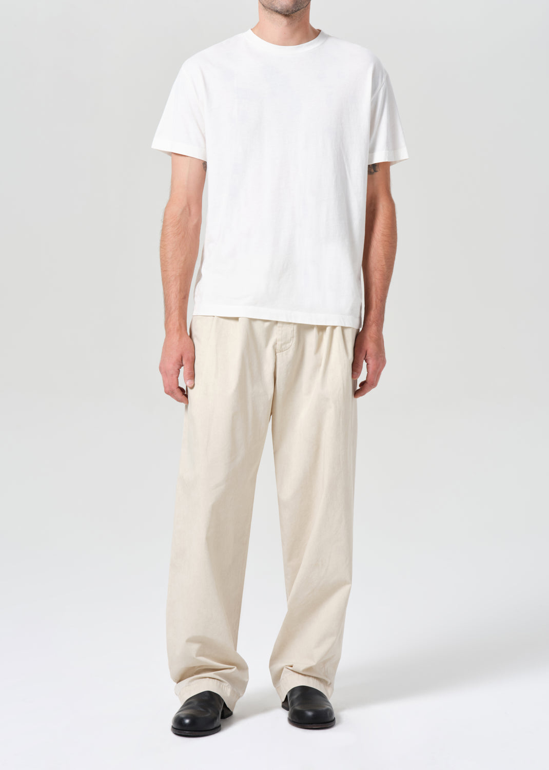 Person wearing a white t-shirt and beige pants on a plain background