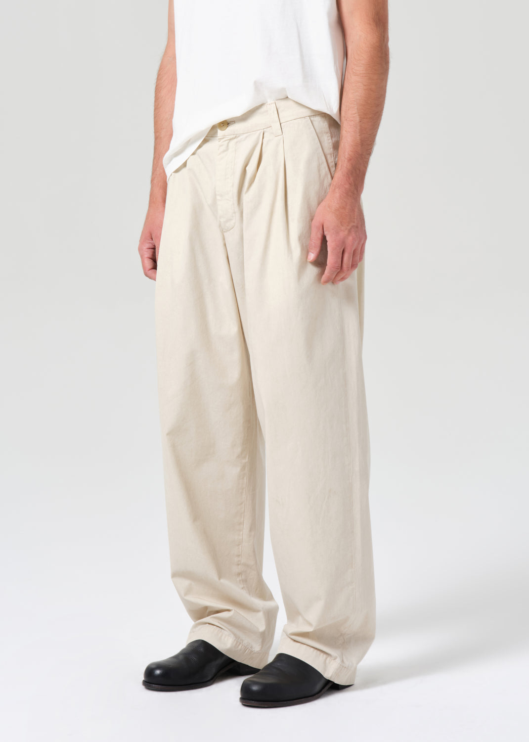 Person wearing beige wide-leg pants and black shoes on a white background