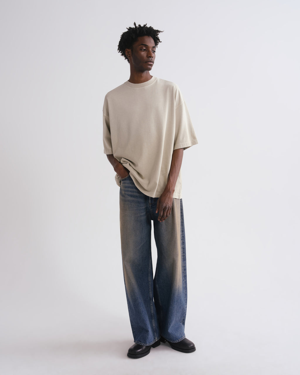 Man wearing a beige sweater and blue jeans on a grey background