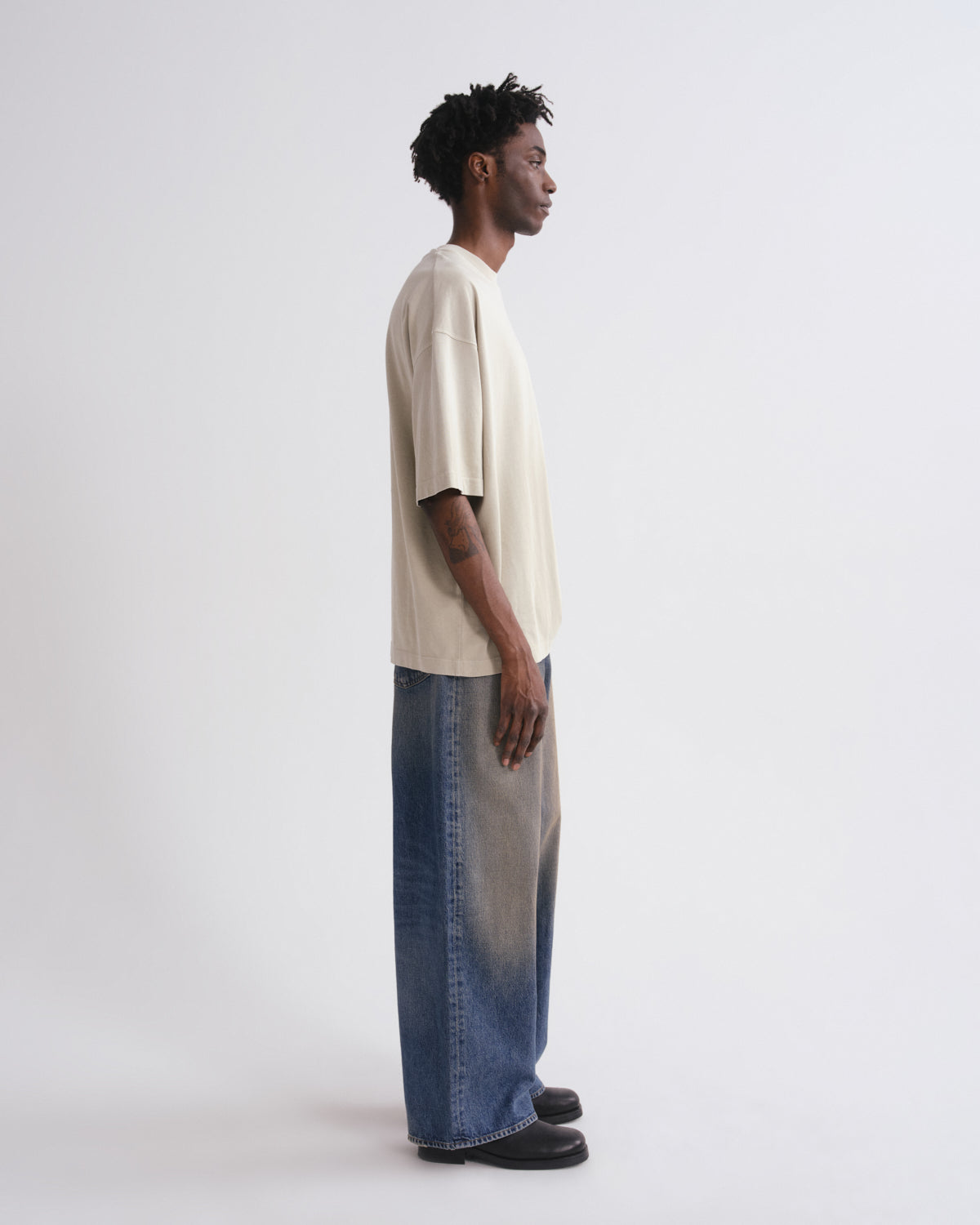 Person wearing a white oversized shirt and blue jeans on a grey background