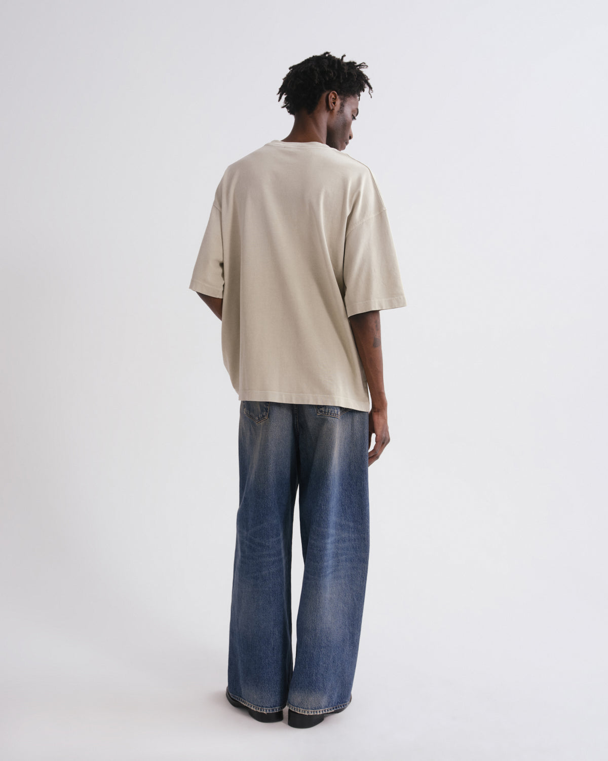 Person wearing a beige oversized t-shirt and blue jeans on a grey background