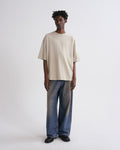 Person wearing a beige t-shirt and blue jeans on a grey background