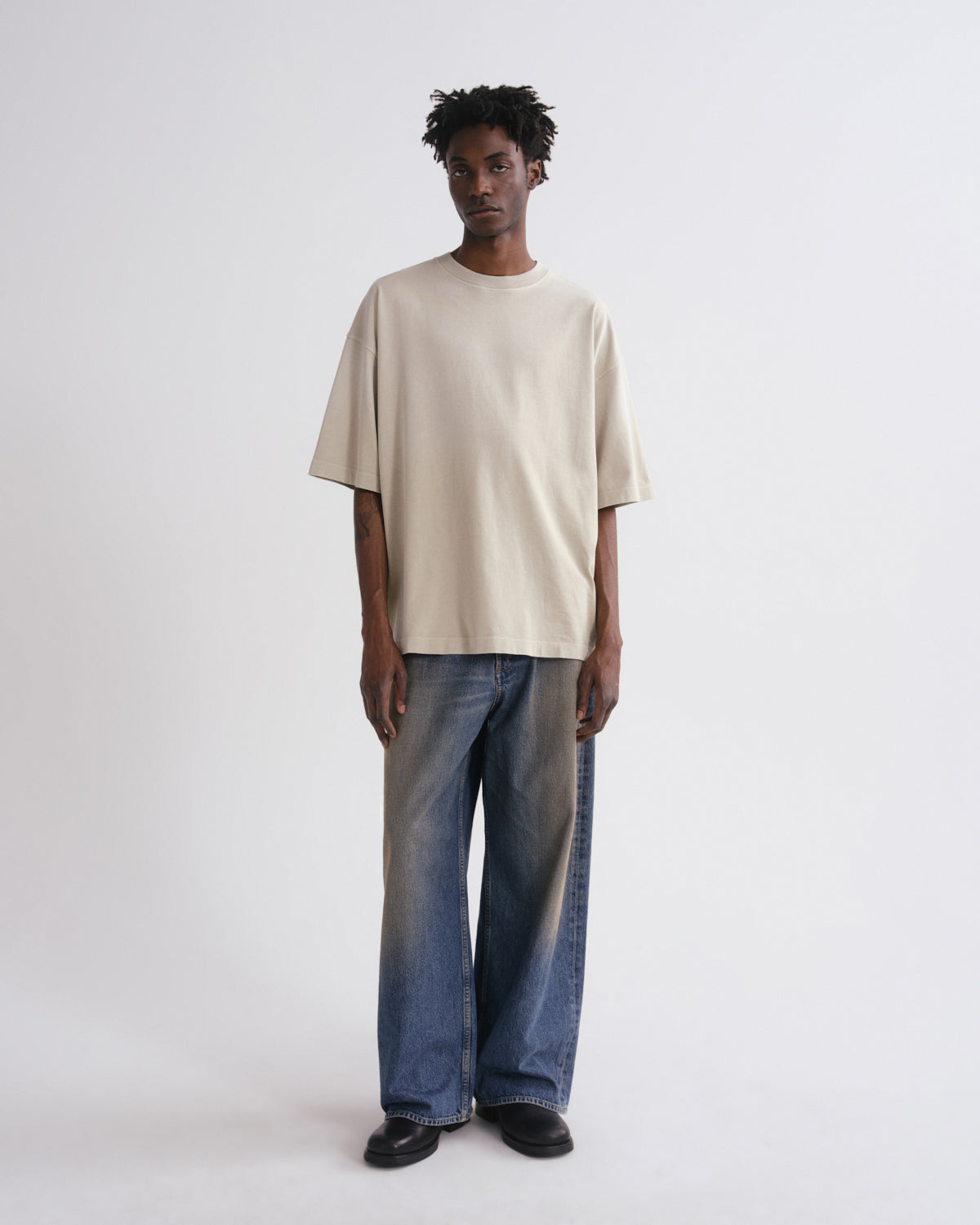 Person wearing a beige t-shirt and blue jeans on a grey background