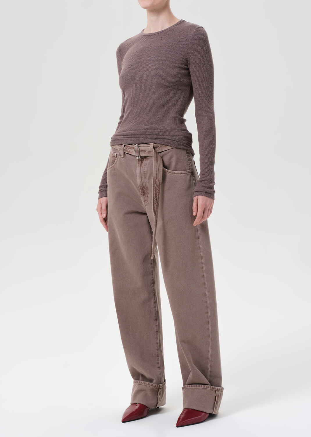Person wearing a brown long-sleeve top and beige pants on a white background
