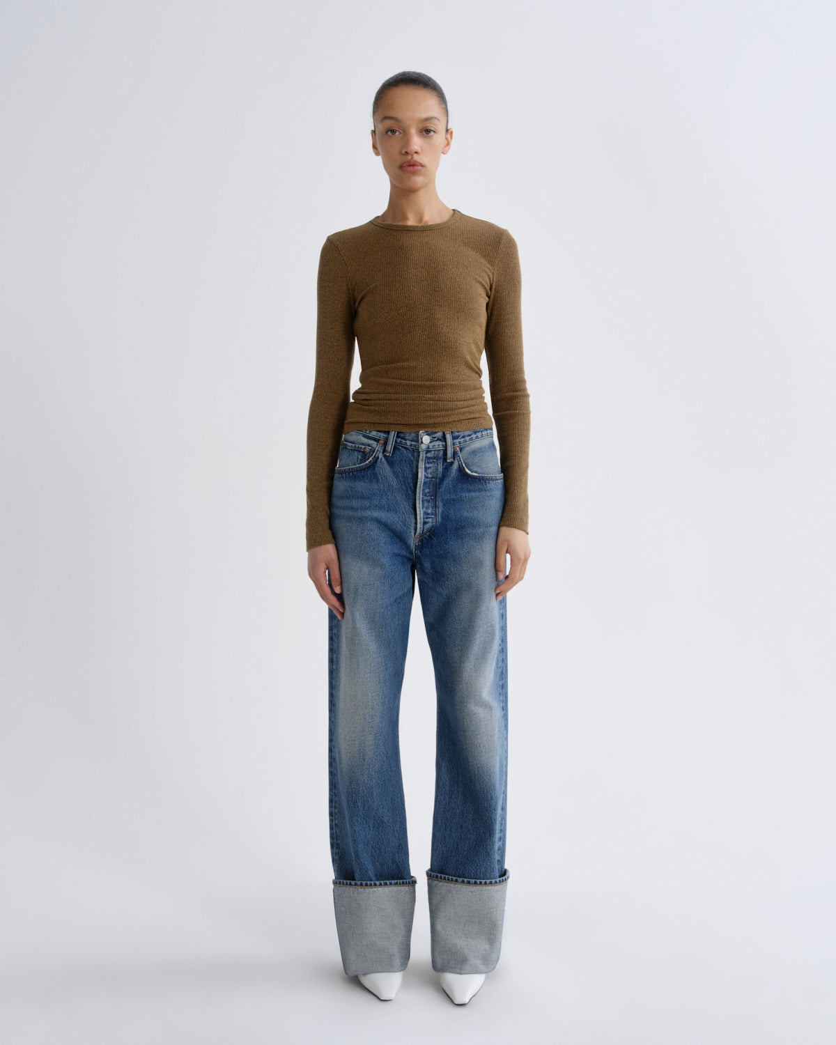 Person wearing a brown long-sleeve top and blue jeans on a white background