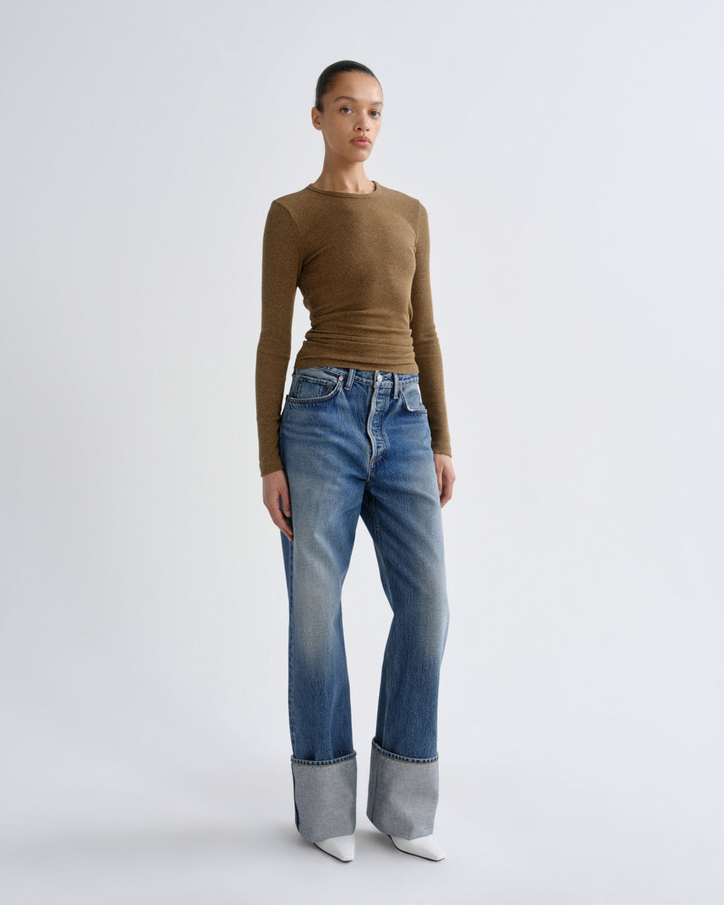 Woman wearing a brown long-sleeve top and blue jeans on a white background