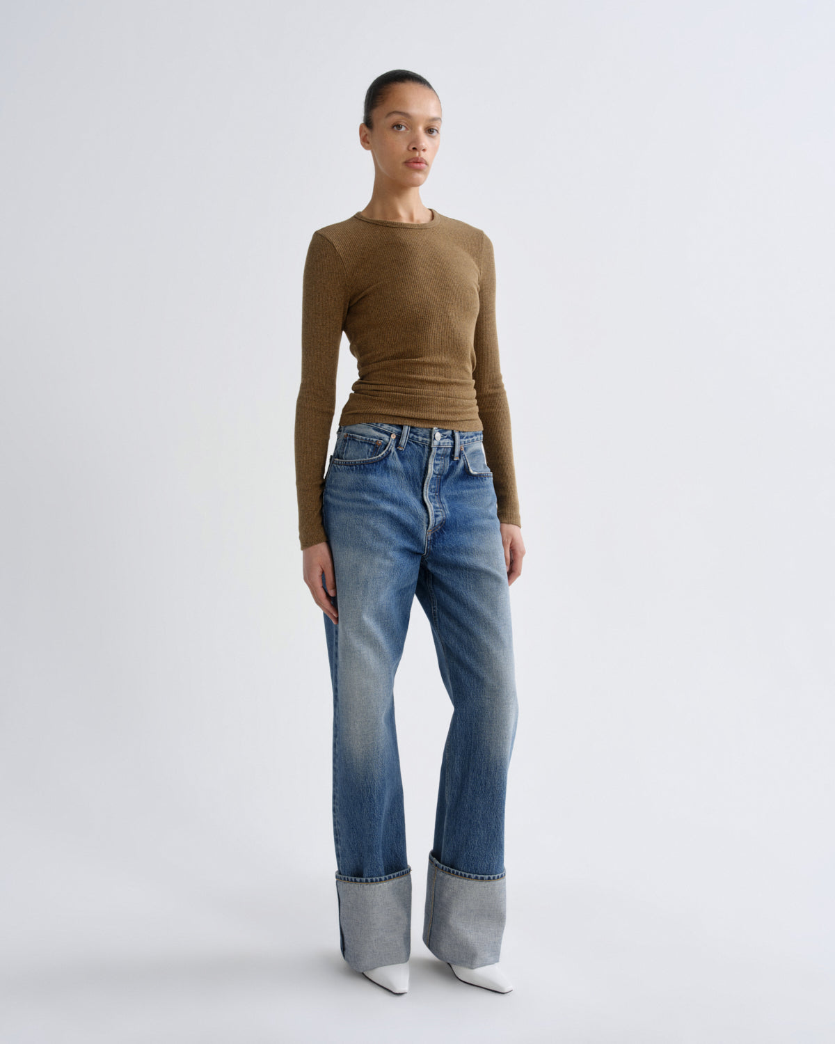 Woman wearing a brown long-sleeve top and blue jeans on a white background