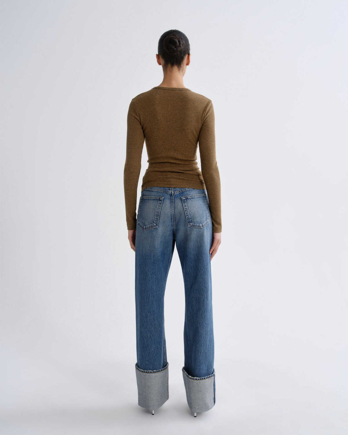 Person wearing a brown sweater and blue jeans with cuffed hems on a white background