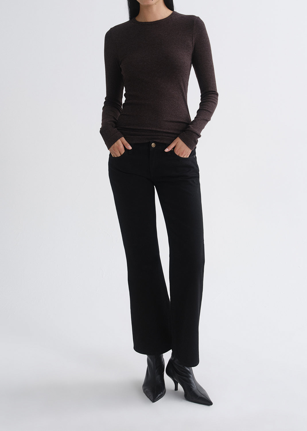 A model wearing a dark brown long-sleeve crewneck knit top, black wide-leg cropped pants, and black pointed-toe ankle boots, standing against a grey background.