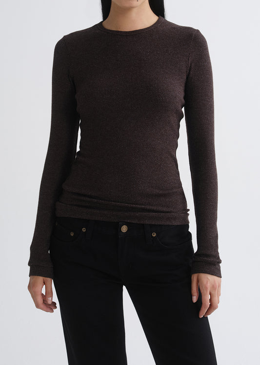 A woman wearing a dark brown ribbed long-sleeve crewneck sweater and black jeans, shown from the neck down against a grey background.