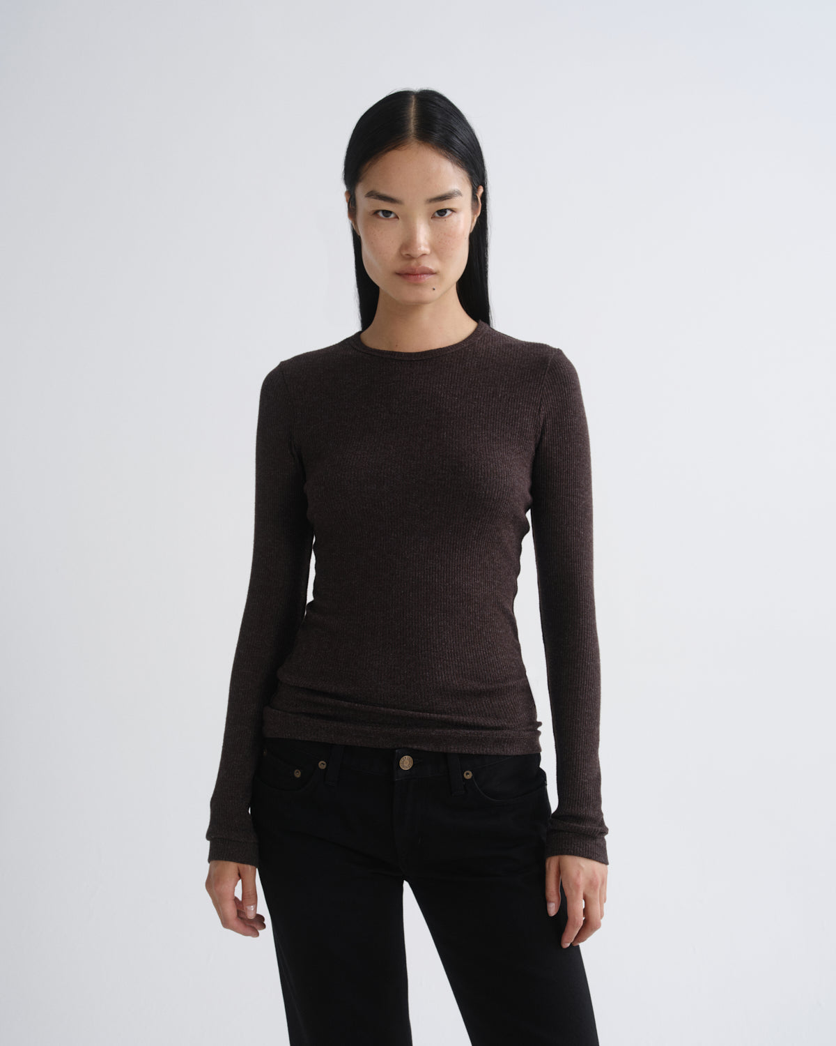 A woman modeling a dark brown long-sleeve crewneck knit top paired with black pants, photographed against a light gray studio background.