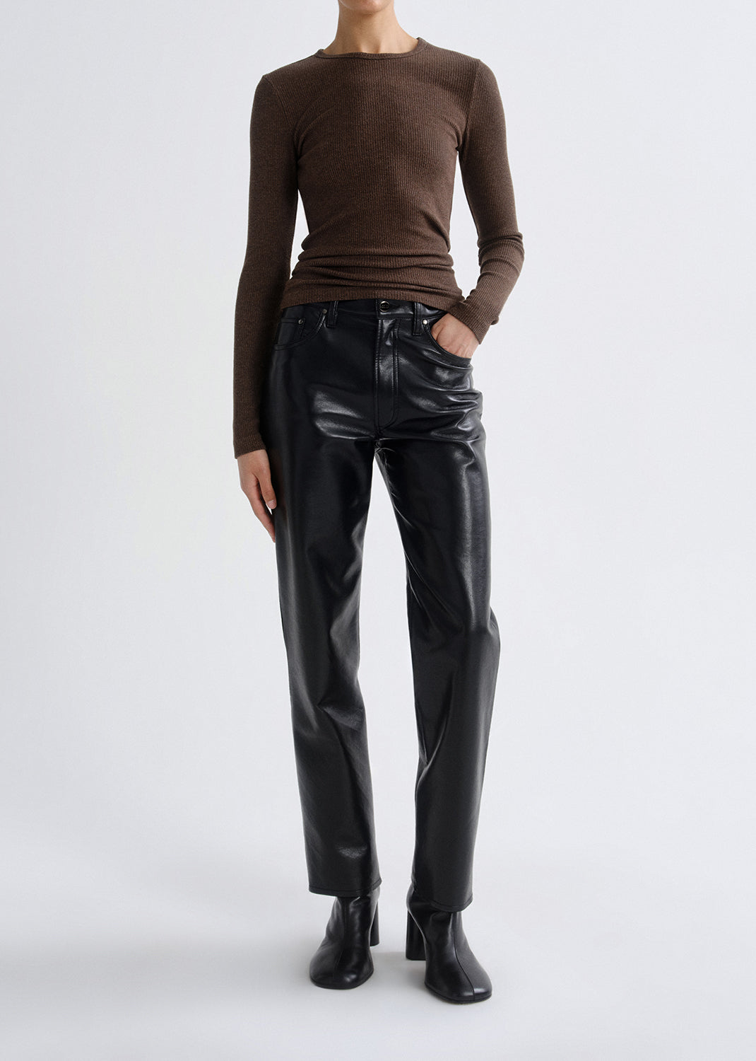 Person wearing a brown long sleeve ribbed top with black leather pants on a grey background.